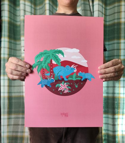 A3 Bright and bold illustration of a blue triceratops family under a palm tree and surrounded by prehistoric plants on a soft pink background.