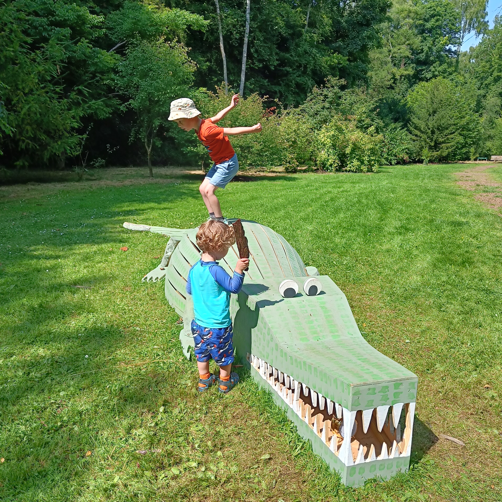 Children jumping off and playing with a wooden crocodile at Evenley Wood Gardens