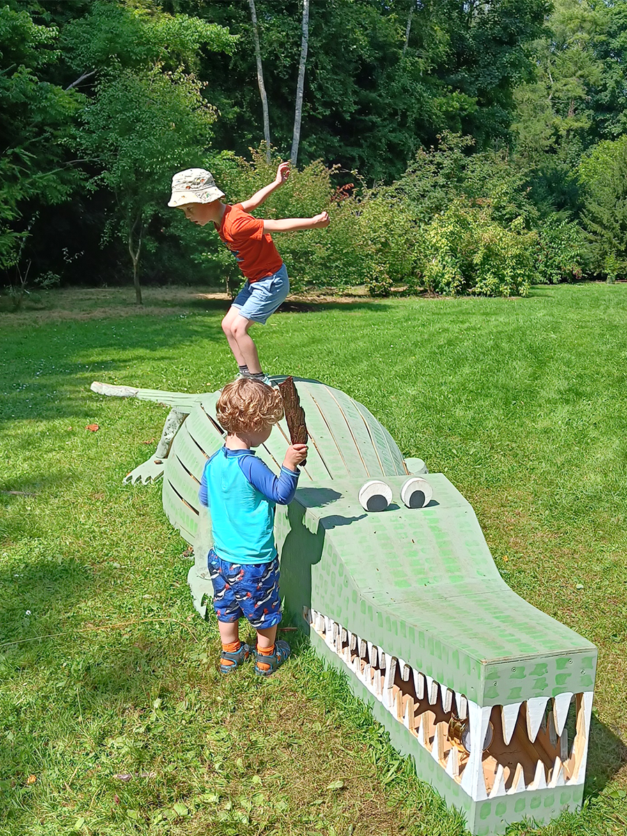 little boys playing with a wooden model of a green painted crocodile at evenley wood garden