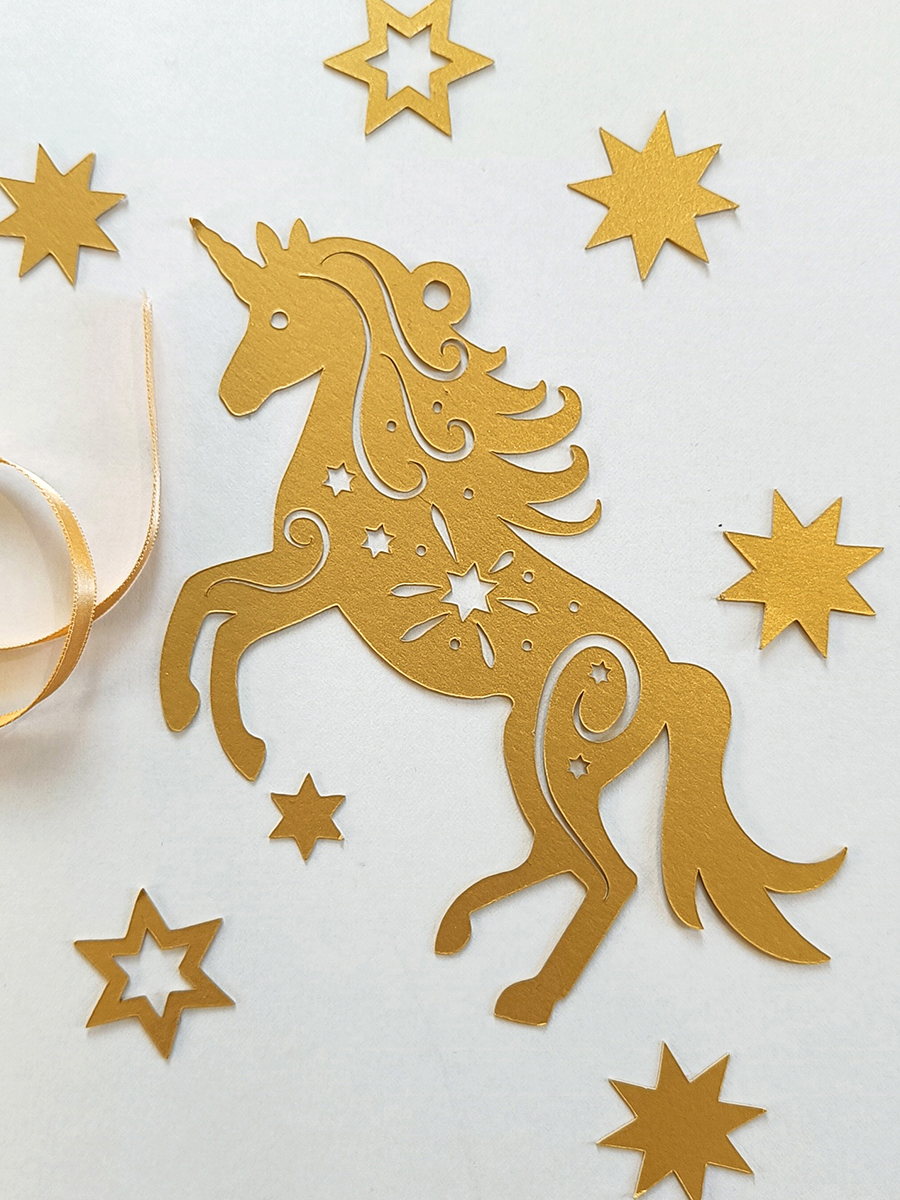 Frosted gold paper cut unicorn decoration with golden stars and ribbon surrounding.