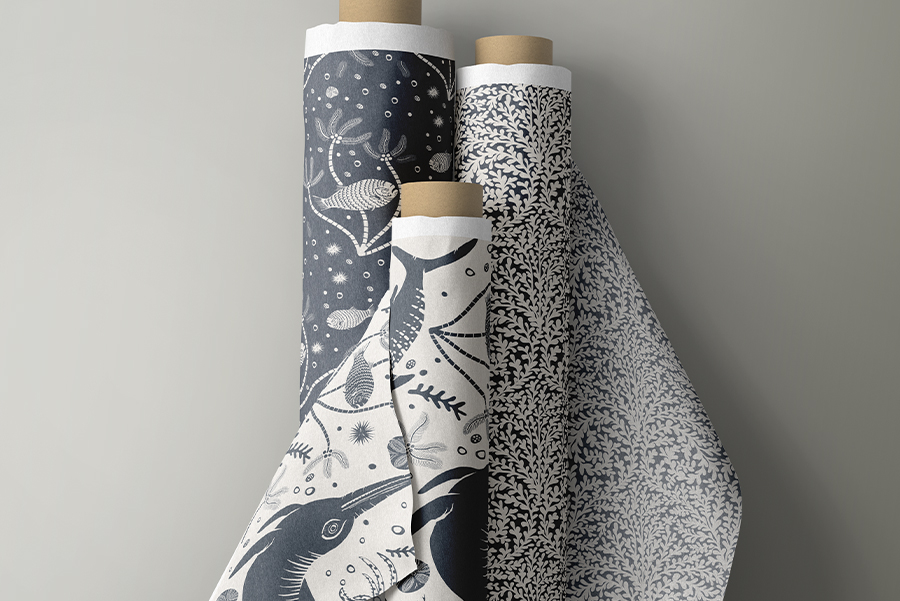 Fabric rolls of Curious Kin's ancient tides collection including icthyosaur, prehistoric fish, and seaweed collections printed in slate blue and cream. Designed by Curious Kin.
