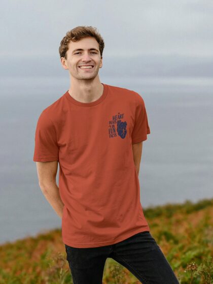 Man on cliff near ocean wearing Curious Kin's my heart beats in fun facts design printed on rust red t-shirt
