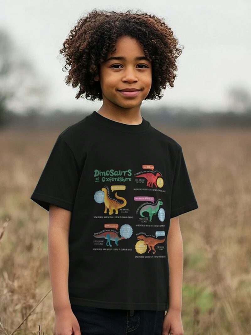 Boy stood in a field wearing a black t-shirt with Curious Kin's dinosaurs of Oxfordshire design printed on it
