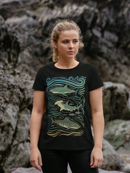 Woman stood in front of rock face wearing a black t-shirt with Curious Kin's shark fun facts design printed on it