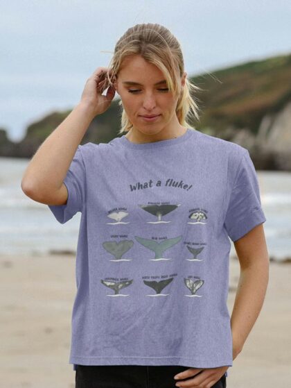 Woman standing on sandy beach wearing Curious Kin's what a fluke t-shirt.