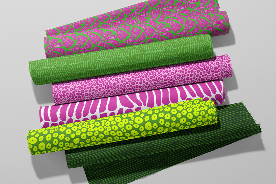 Rolls of fabric featuring patterns designed by Curious Kin in magenta and green tones. Includes abstract polka dotes, stripes and ginkgo leaves.