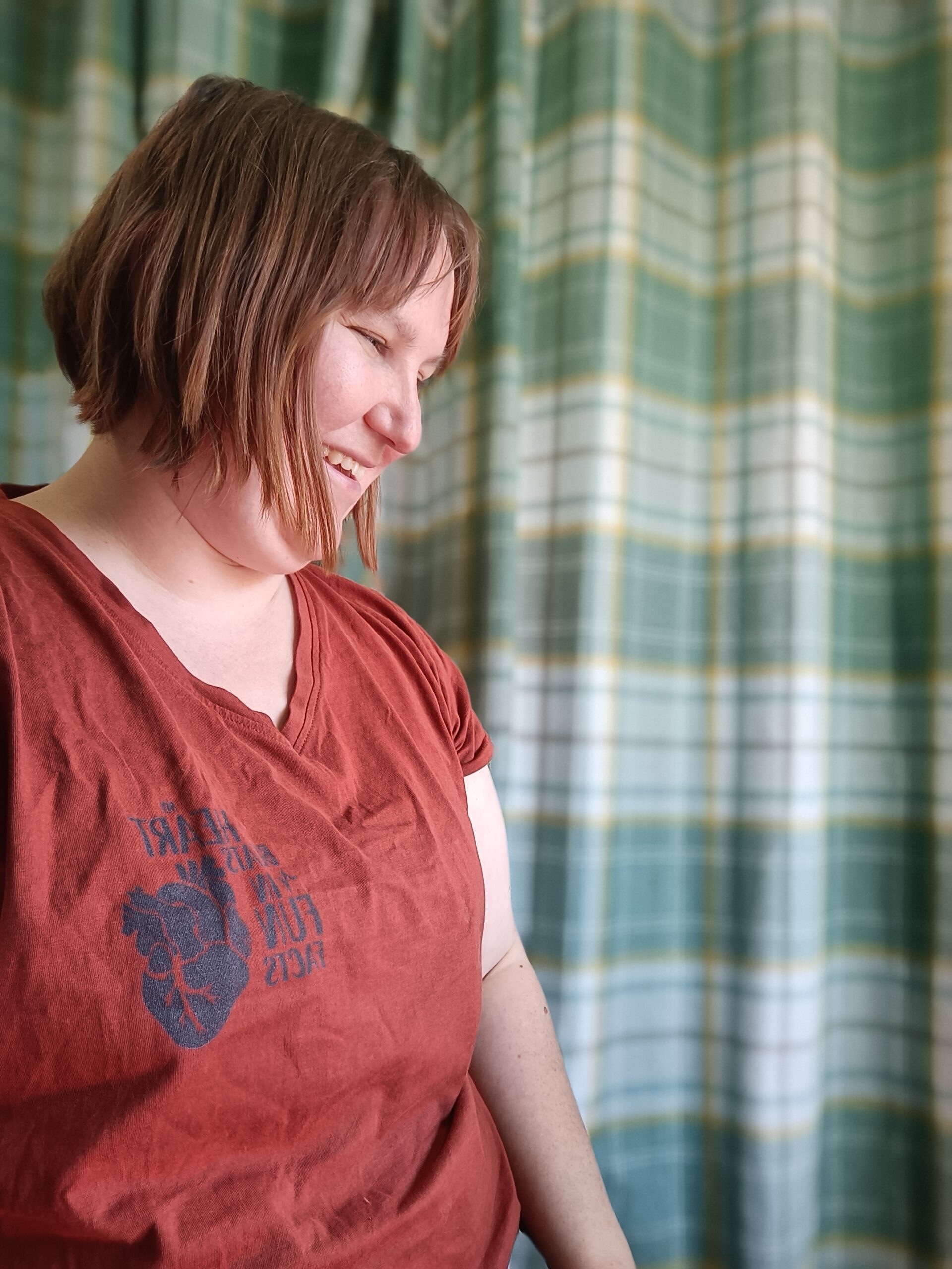 Portrait of Min wearing my heart beats in fun facts t-shirts, sitting smiling and looking downwards.