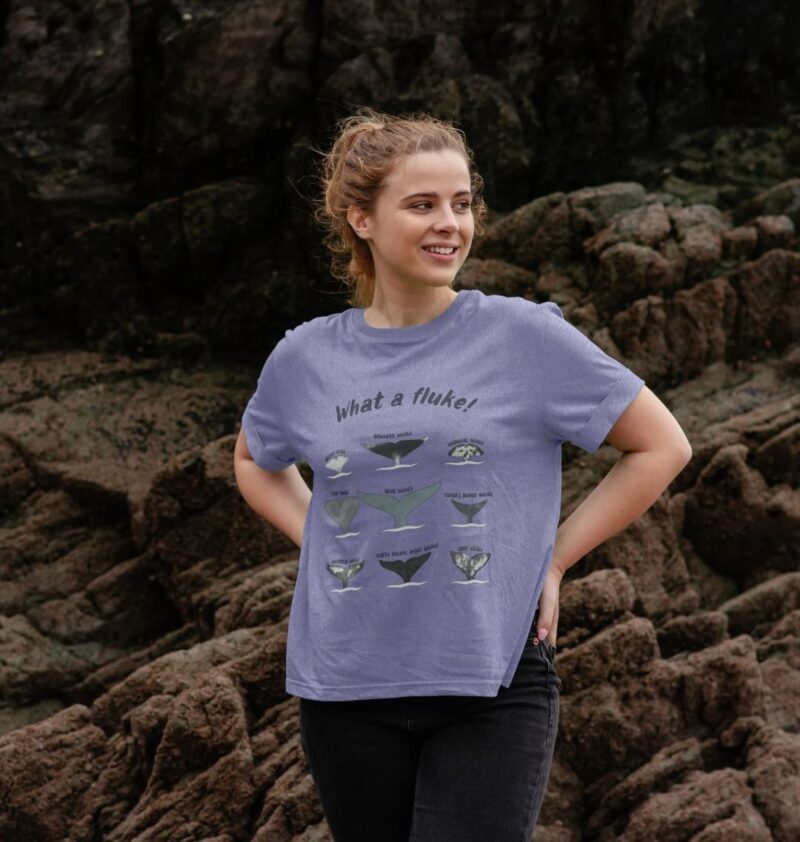 Woman with hands on her hips wearing a lilac relaxed fit womens t-shirt with 9 whale fluke tails and the title what a fluke!