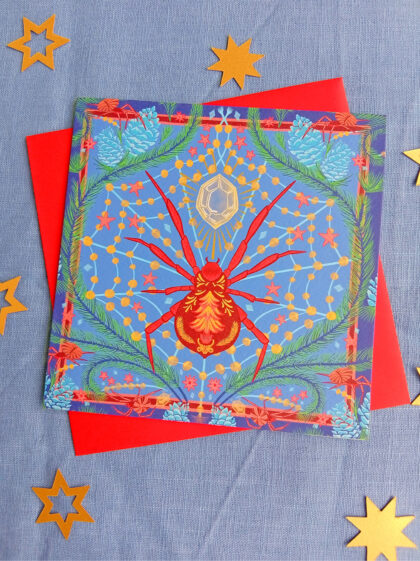 Square Christmas card of a Christmas spider with jewelled web inbetween pine leaves.