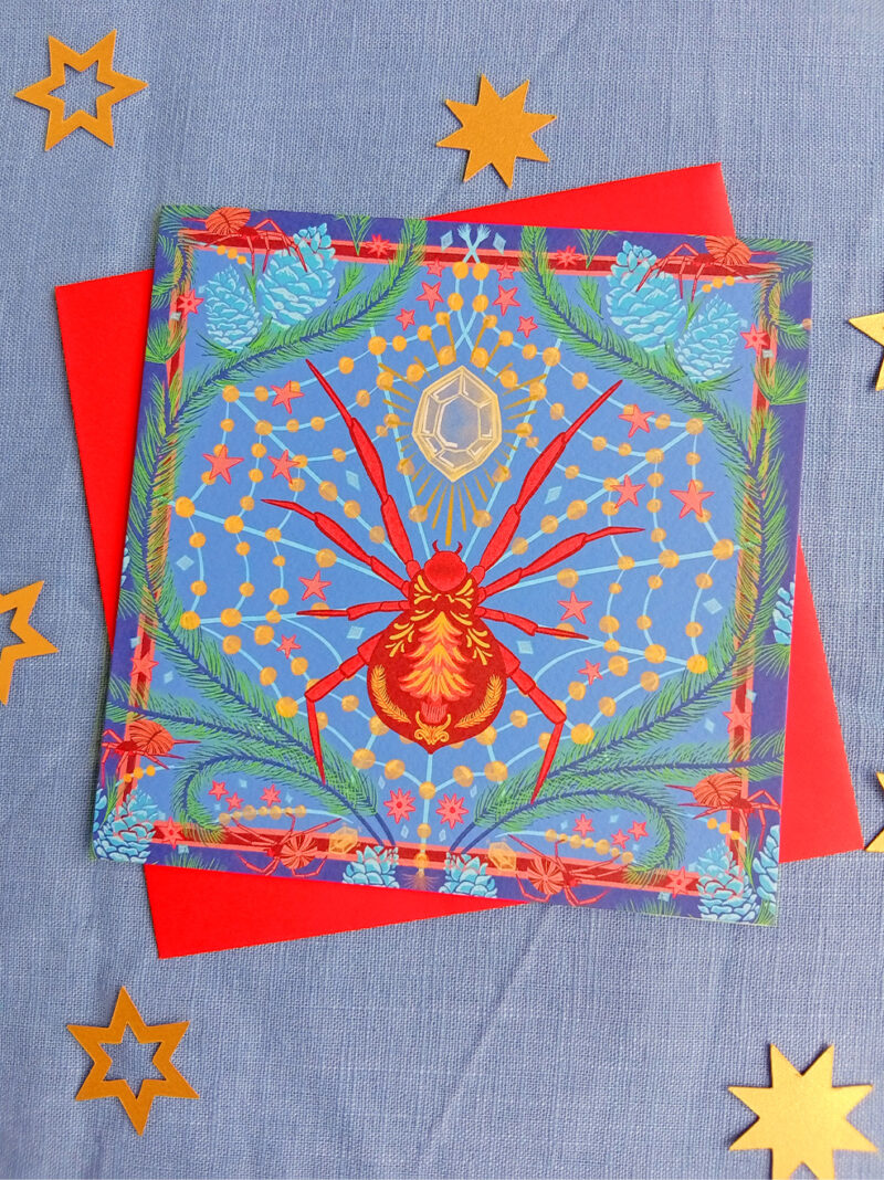 Square Christmas card of a Christmas spider with jewelled web inbetween pine leaves.