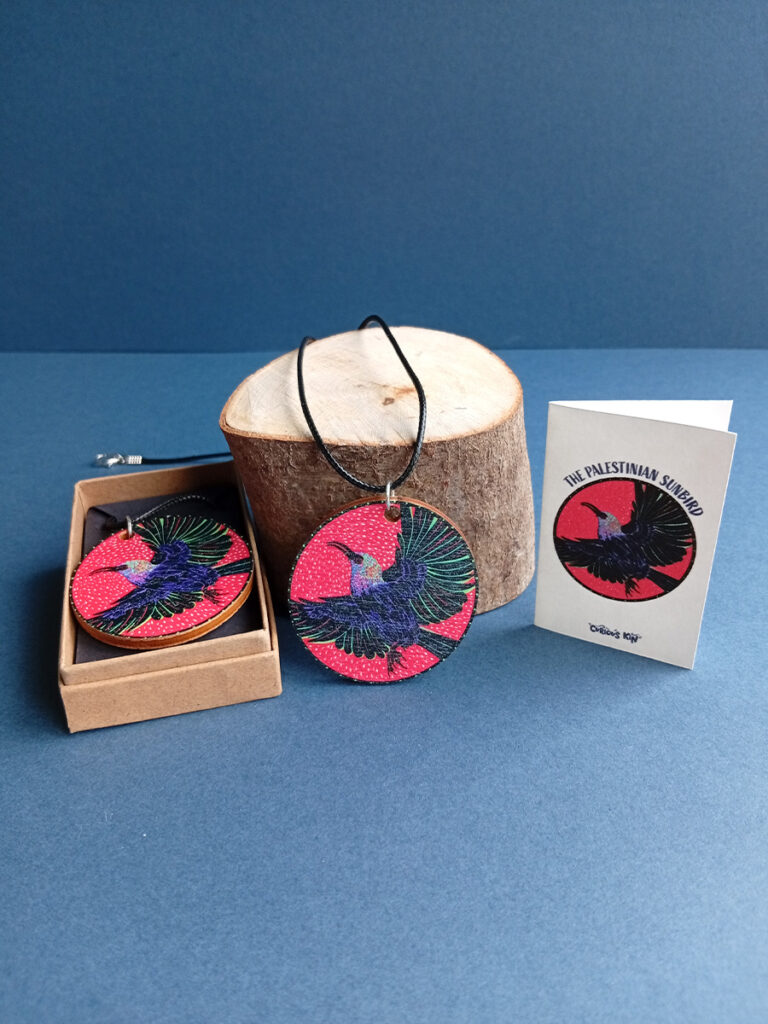 UV printed rounded wooden pendant with illustration of Palestinian Sunbied and a waxed cotton cord, mini card and kraft jewellery box with black card liner.
