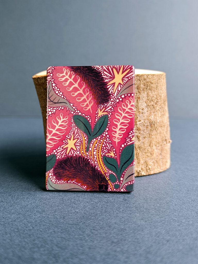 Alaskan woolly bear caterpillar illustrated magnet in red tones balancing against a small wood log.