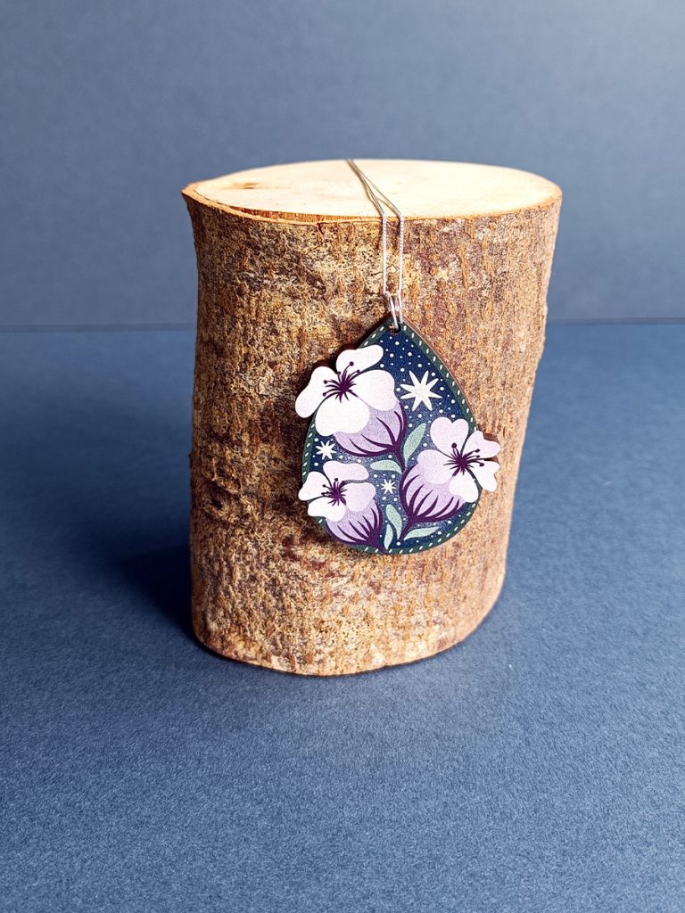 Wooden pear shaped pendant with arctic flower illustration hanging on eco sterling silver fine chain on a log