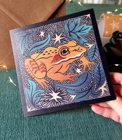 hand holding square card with Alaskan Wood Frog and stars card