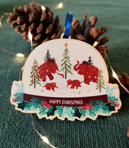 A wooden tree decoration shaped like a snow globe with an illustration of mammoth family having a snowball fight inside snowglobe printed. Wreath and Merry Christmas printed below snow globe. Comes with ribbon tie.