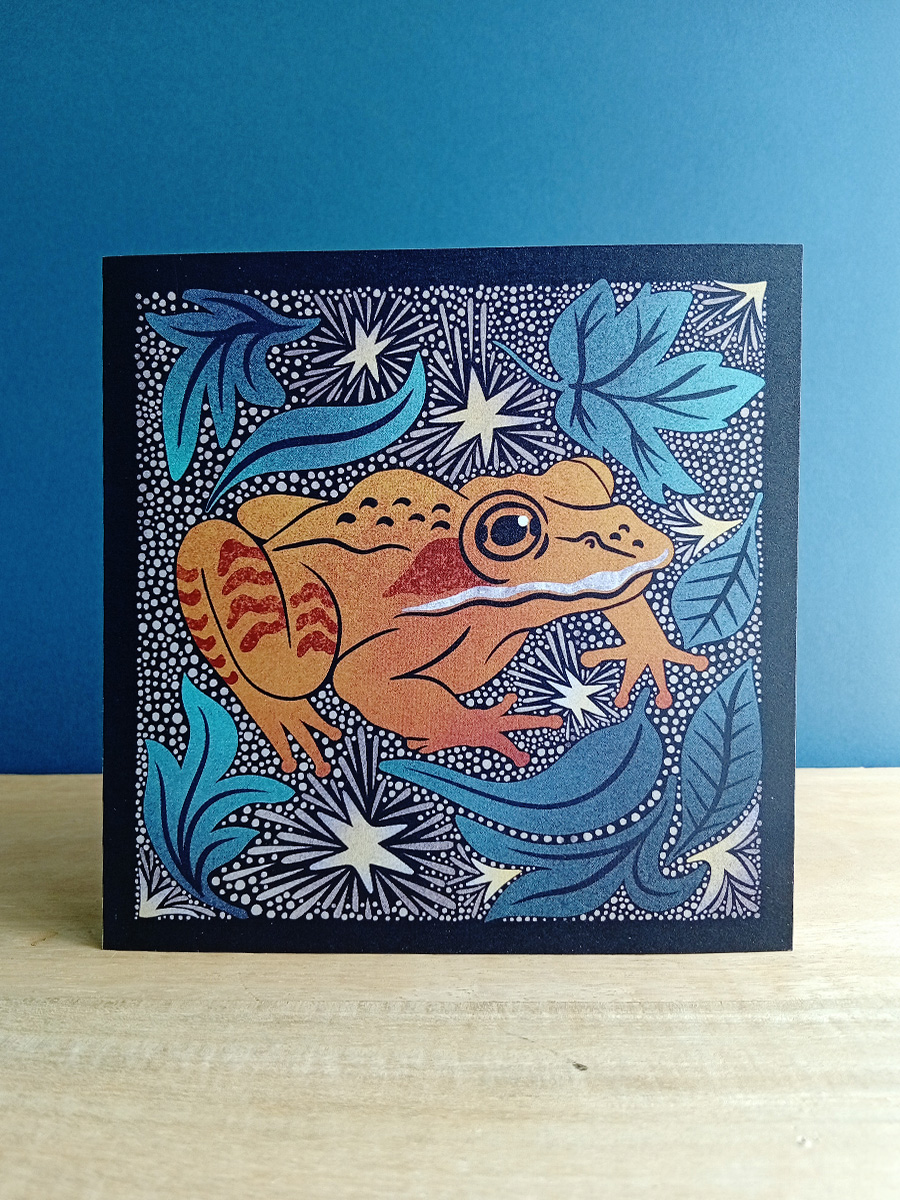 Square linocut inspired illustrated card of an Alaskan wood frog, surrounded by leaf litter and stars.