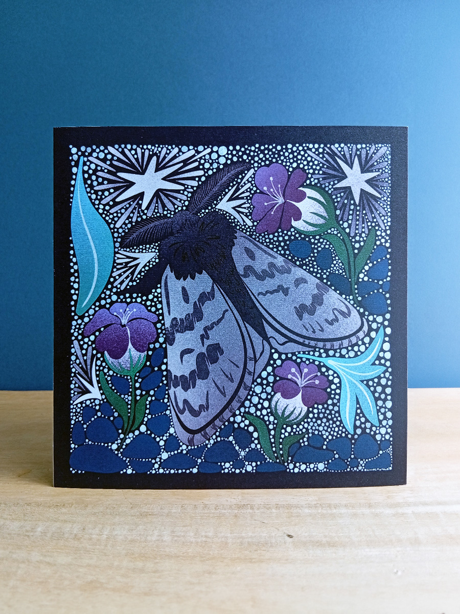 Square card with Arctic woolly bear moth illustrated in a linocut style in soft greys, purples and blues, surrounded by leaf litter and frosted stars.
