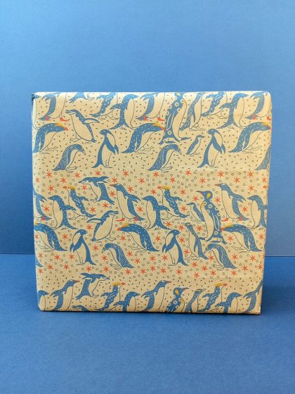 Gift wrapped in recycled wrapping paper with hand drawn parade of penguins hopping between stars in blue and red tones.