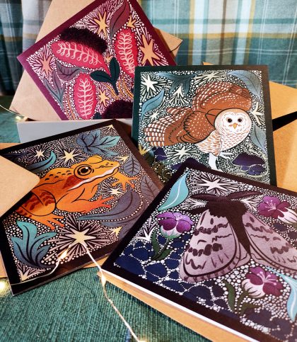 A set of 4 illustrated square winter cards in jewel tones with arctic woolly bear moth, caterpillar, barred owl and alaskan wood frog featured one animal per card.